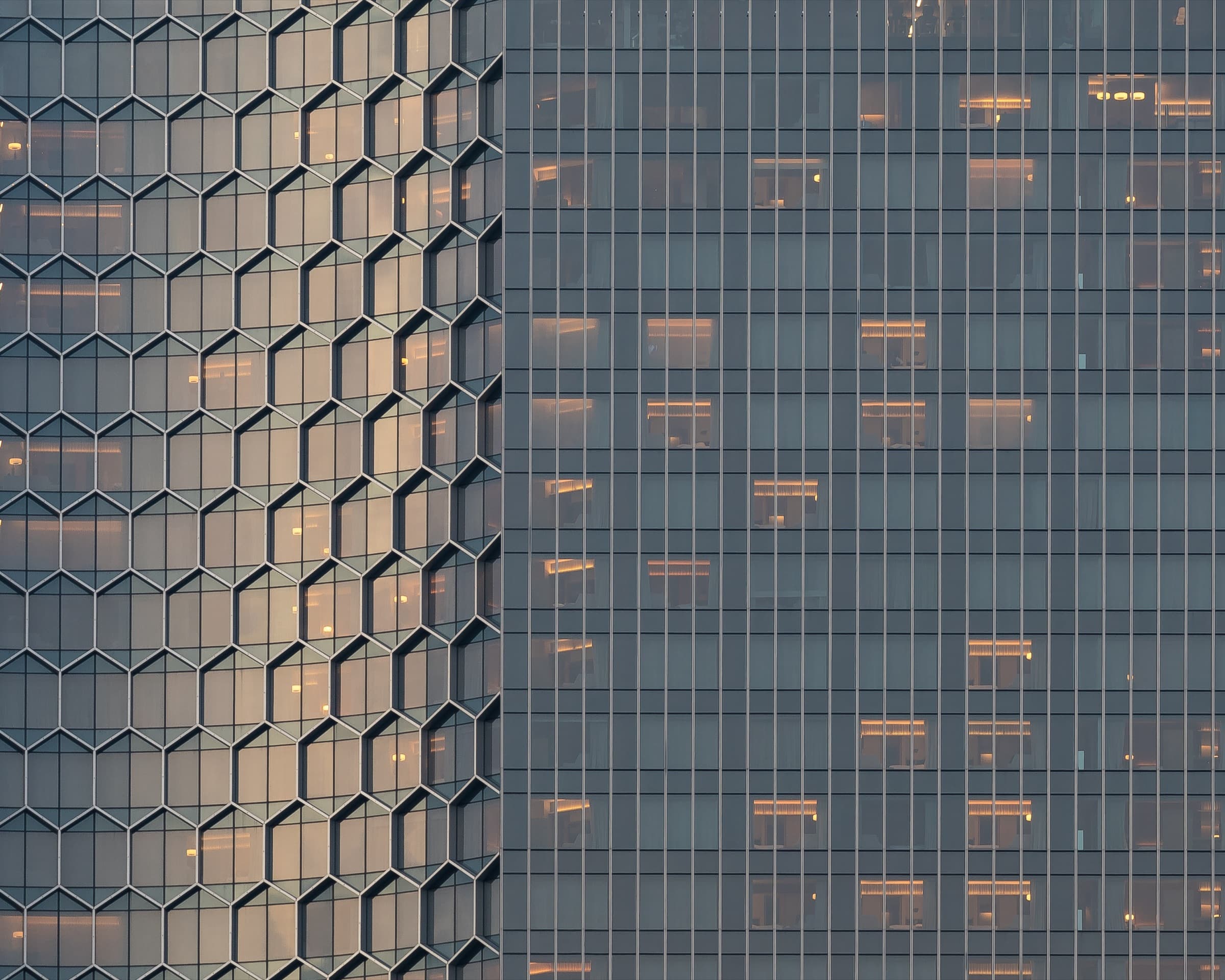 A curved honeycomb glass façade of a high-rise building at sunset
